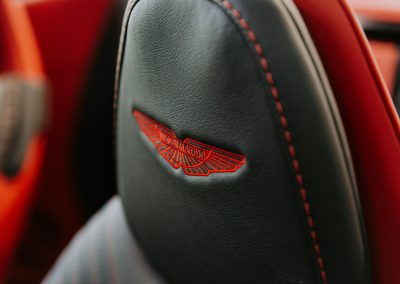 Primer plano de un asiento de coche de lujo con el logotipo de Aston Martin bordado, destacando la exclusividad y el diseño elegante.
