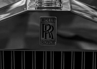 Primer plano de la parte frontal de un Rolls Royce. Se aprecia el logotipo de la marca. Fotografía blanco y negro